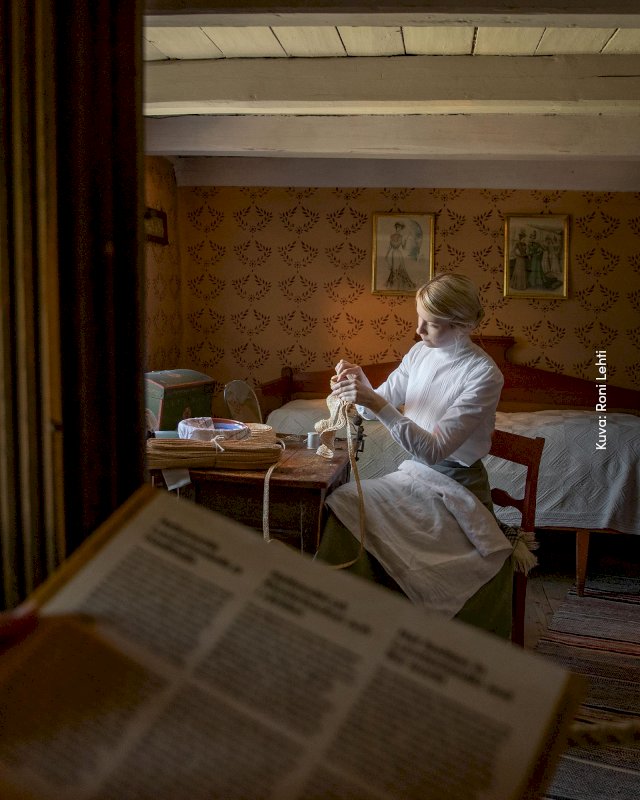 Nainen kutomassa vanhassa tuvassa.